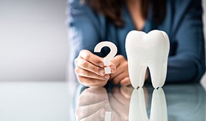 Woman holding a question mark next to a large model tooth on a reflective surface