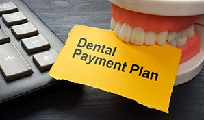 Set of artificial teeth holding a yellow paper that says, “Dental Payment Plan”